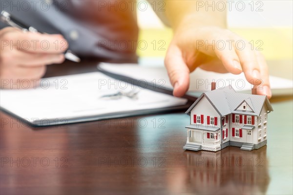 Man signing real estate contract papers and reaching for small model home in front