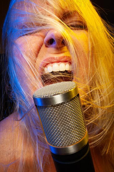 Female vocalist under gelled lighting sings with passion into condenser microphone