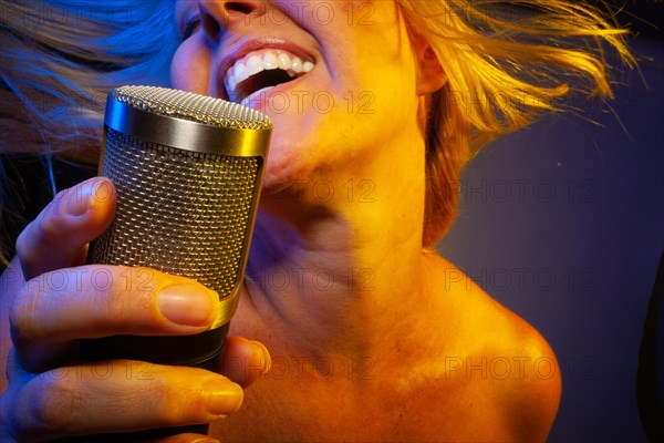 Female vocalist under gelled lighting sings with passion into condenser microphone