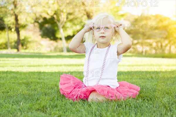 Cute little girl playing dress in the grass up with pink glasses and beaded necklace