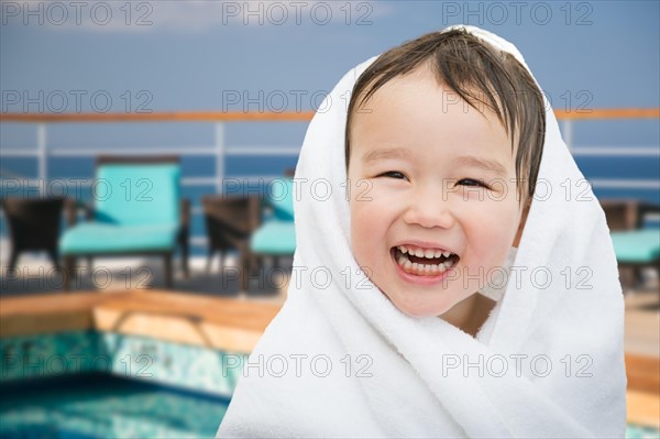 Happy cute mixed-race chinese and caucasian boy on cruise ship wrapped in A towel