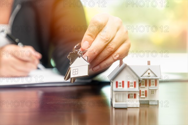 Woman signing real estate contract papers holding house keys and home keychain with small model home in front