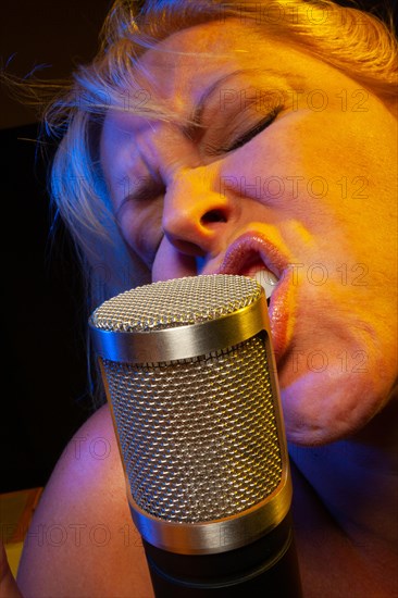 Female vocalist under gelled lighting sings with passion into condenser microphone