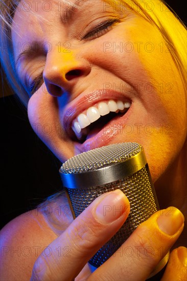 Female vocalist under gelled lighting sings with passion into condenser microphone