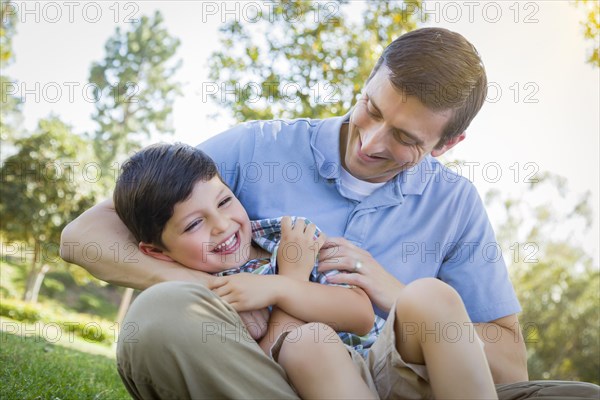 Loving young father tickling son in the park