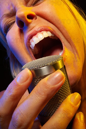 Female vocalist under gelled lighting sings with passion into condenser microphone