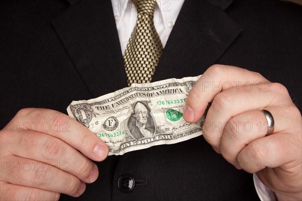 Businessman with coat and tie holding wrinkled United States dollar bill