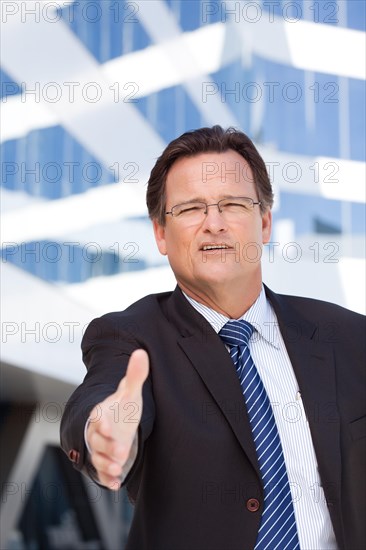 Handsome businessman in suit and tie holds out his hand to shake outside of corporate building
