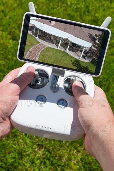 Hands holding drone quadcopter controller with overhead of house on screen