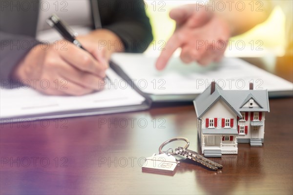 Real estate agent and customer sign contract papers with house keys and small model home in front