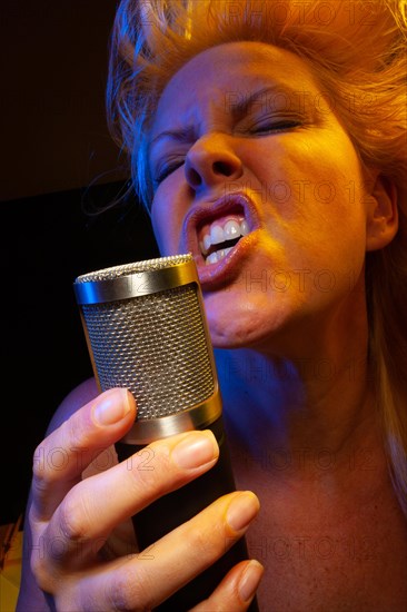 Female vocalist under gelled lighting sings with passion into condenser microphone