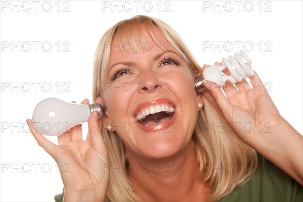 Funny faced woman holds energy saving and regular light bulbs to her ears isolated on a white background
