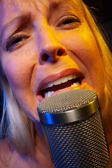 Female vocalist under gelled lighting sings with passion into condenser microphone