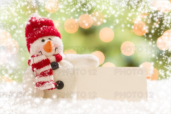 Cute snowman with scarf and hat next to blank white card over abstract snow and light background