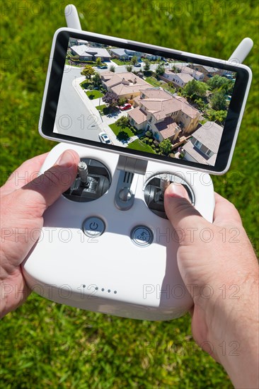 Hands holding drone quadcopter controller with residential homes on screen