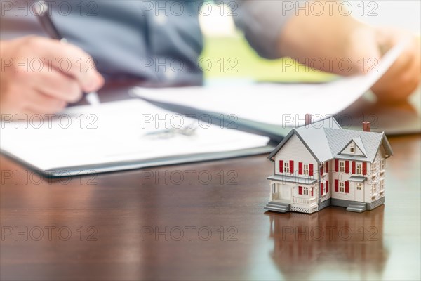 Man signing real estate contract papers with small model home in front