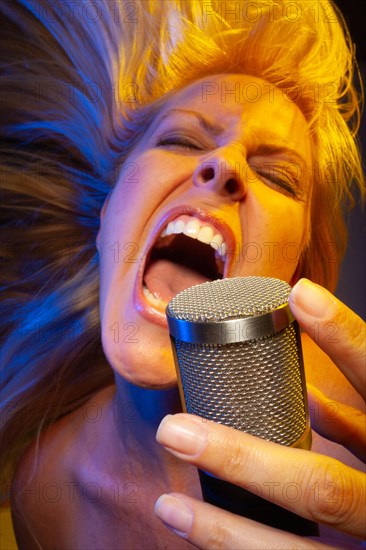 Female vocalist under gelled lighting sings with passion into condenser microphone