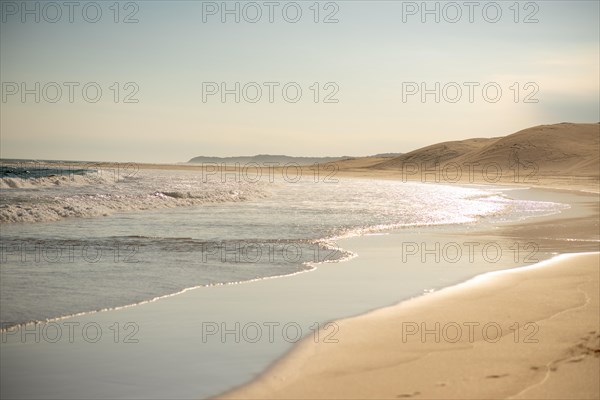 Waves crashing into coast with sand dunes in background