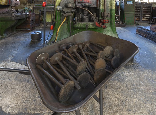 Car valves in the raw state in a wheelbarrow in front of a screw press in a drop forge