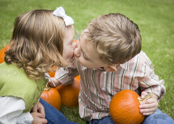 Cute young brother and sister children kissing among the pumpkins at the pumpkin patch