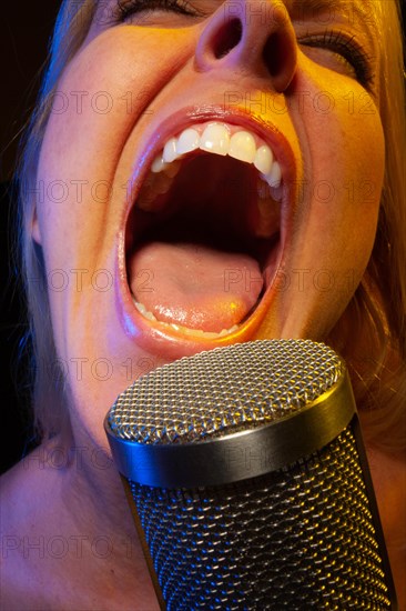 Female vocalist under gelled lighting sings with passion into condenser microphone