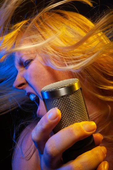 Female vocalist under gelled lighting sings with passion into condenser microphone