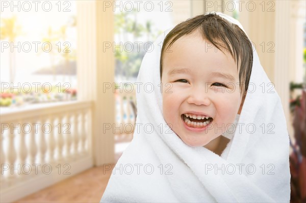 Happy cute mixed-race chinese and caucasian boy on tropical patio wrapped in A towel