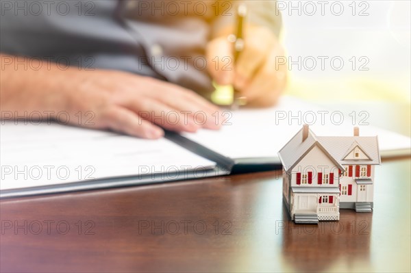 Man signing real estate contract papers with small model home in front