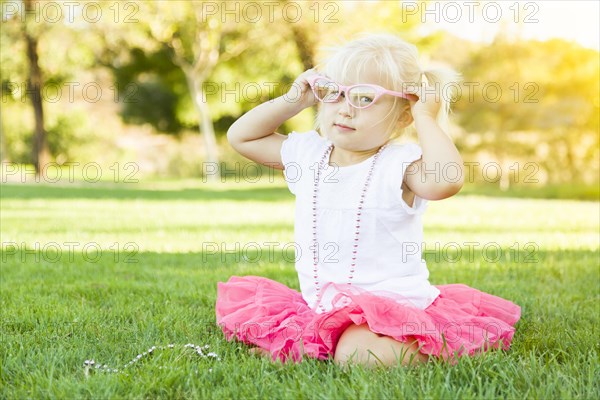 Cute little girl playing dress in the grass up with pink glasses and beaded necklace