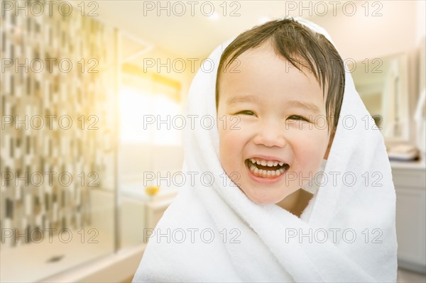 Happy cute mixed-race chinese and caucasian boy in bathroom wrapped in A towel