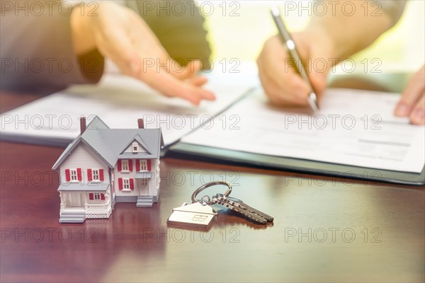 Real estate agent and customer sign contract papers with house keys and small model home in front