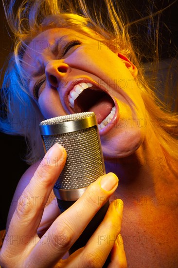 Female vocalist under gelled lighting sings with passion into condenser microphone