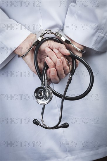 Female doctor or nurse in handcuffs and lab coat holding stethoscope