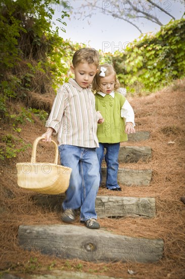 Adorable brother and sister children holding hands walking down wood steps with basket outside