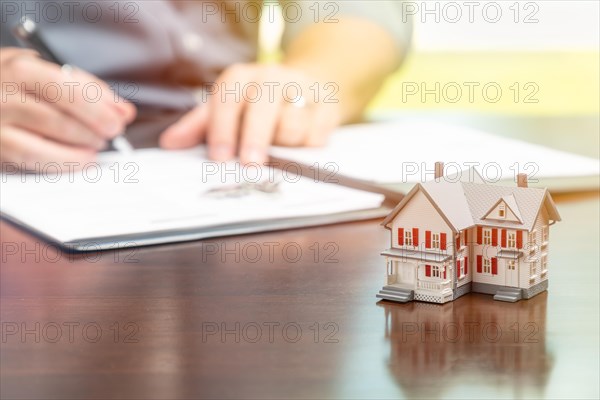 Man signing real estate contract papers with small model home in front