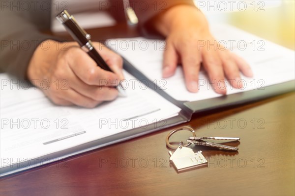 Woman signing real estate contract papers with house keys and home keychain in front