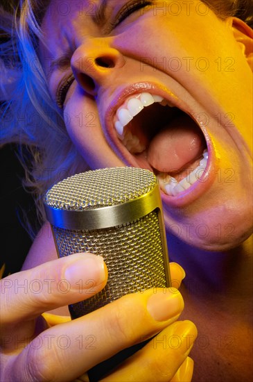 Female vocalist under gelled lighting sings with passion into condenser microphone