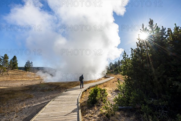 Hiker on footbridge next to steaming hot spring