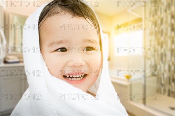 Happy cute mixed-race chinese and caucasian boy in bathroom wrapped in A towel