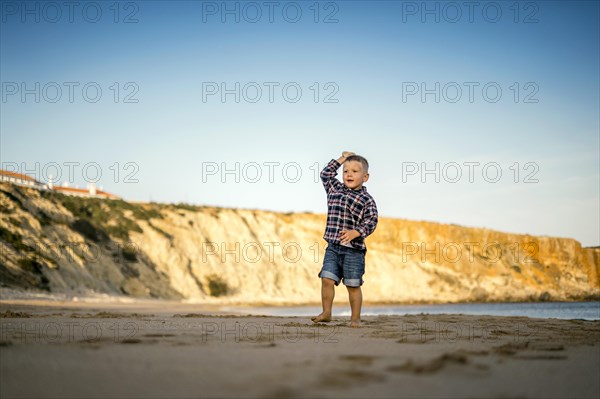 Small boy throwing stones on the beach by the sunset