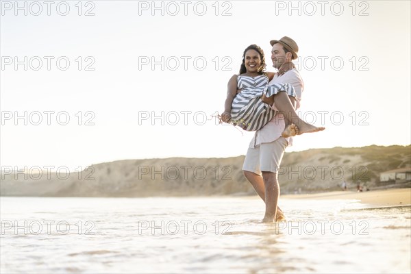 A young man carrying his beloved woman on the beach by sunset in Algarve