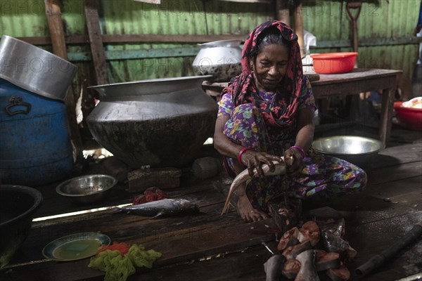 A woman sits on the floor of a cookshop scaling a fish