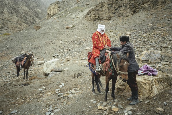 A man helps his pregnant woman onto a horse