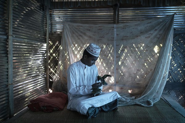 Ahmed on a raffia rug on the floor of a hut playing with two birds