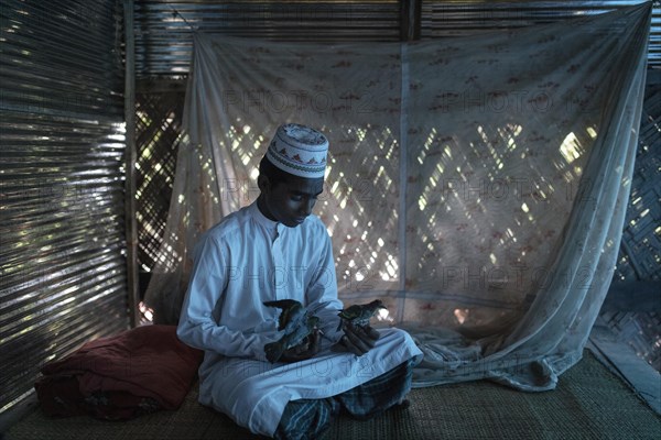 Ahmed on a raffia rug on the floor of a hut playing with two birds