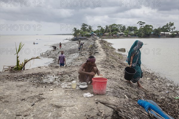 A man sieves river water from wash bowls on a muddy embankment