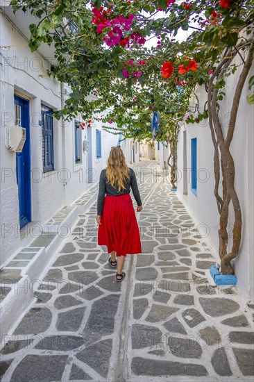 Young woman with dress walking through alley with Cycladic houses