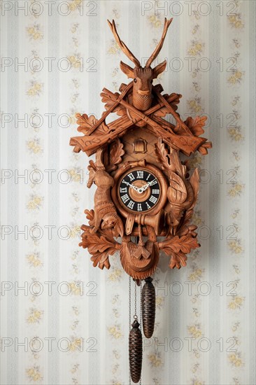 Old black forest cuckoo clock in front of old fashioned wallpaper wall