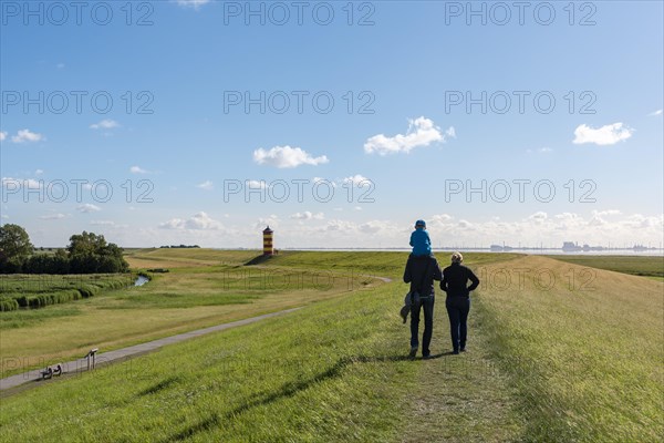 Young family walking on the high water dam near the Pilsum lighthouse