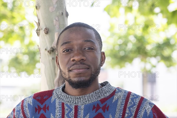 Young black man sitting on bench with African poncho